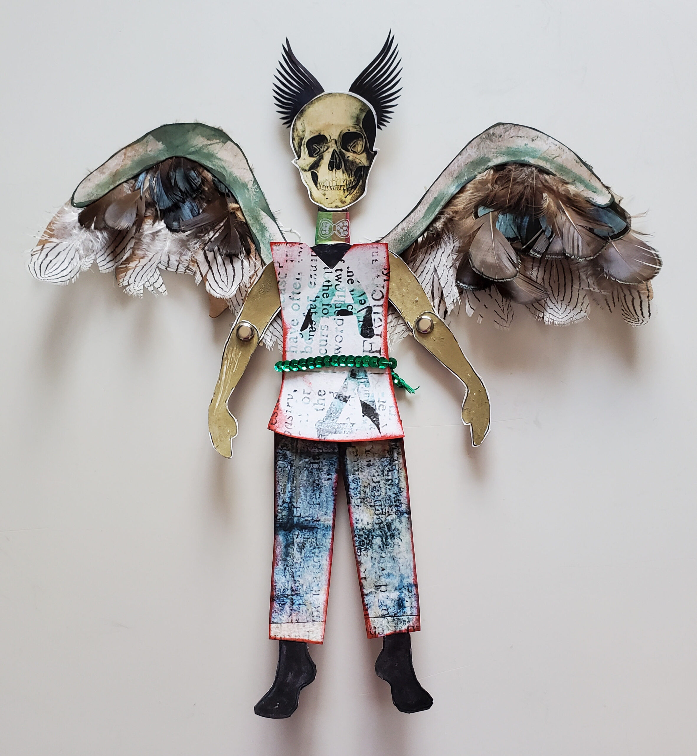 A cardnoard articulated figure of The Teacher. Skull for head, hair that looks like horns, and daemon wings with real feathers.